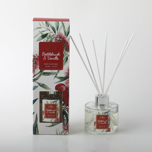 clear round glass bottle with silver collar; white reed sticks; decorative box with bottlebrush flower and red parrot artwork; red label with white text on bottle and box;