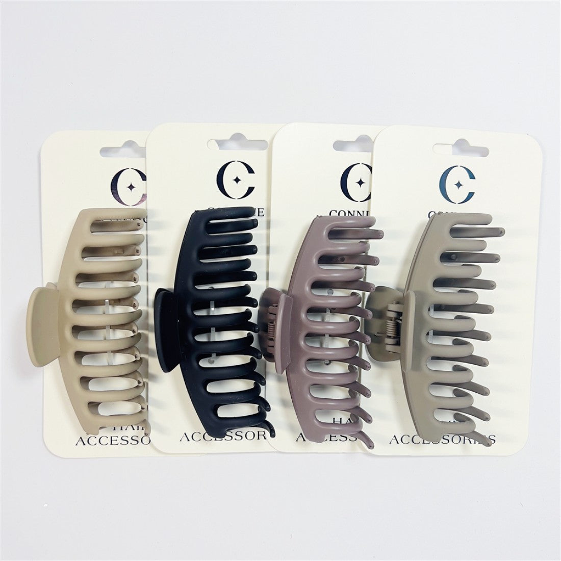 Large plastic hair claw clips on branded backing cards; Matte finish in neutral colours including beige, black and taupe; Curved keel-shaped body with wide spaced teeth; Spring hinge mechanism at centre of clip;