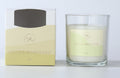 Clear glass candle holder; White wax with single wick; Yellow and cream labelled packaging; Label with floral design and branding; Light yellow and cream colour scheme;