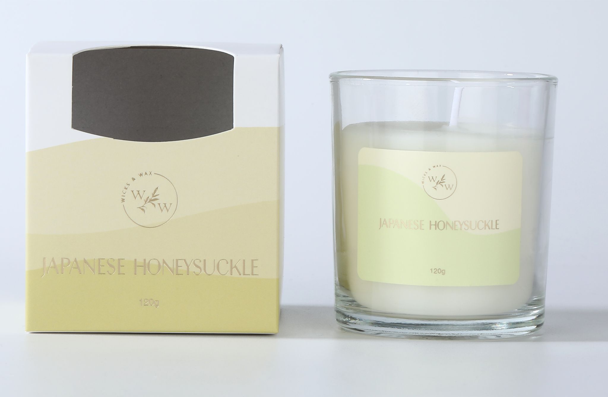 Clear glass candle holder; White wax with single wick; Yellow and cream labelled packaging; Label with floral design and branding; Light yellow and cream colour scheme;