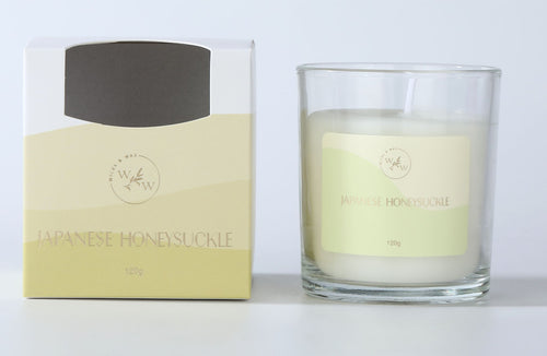 Clear glass candle holder; White wax with single wick; Yellow and cream labelled packaging; Label with floral design and branding; Light yellow and cream colour scheme;