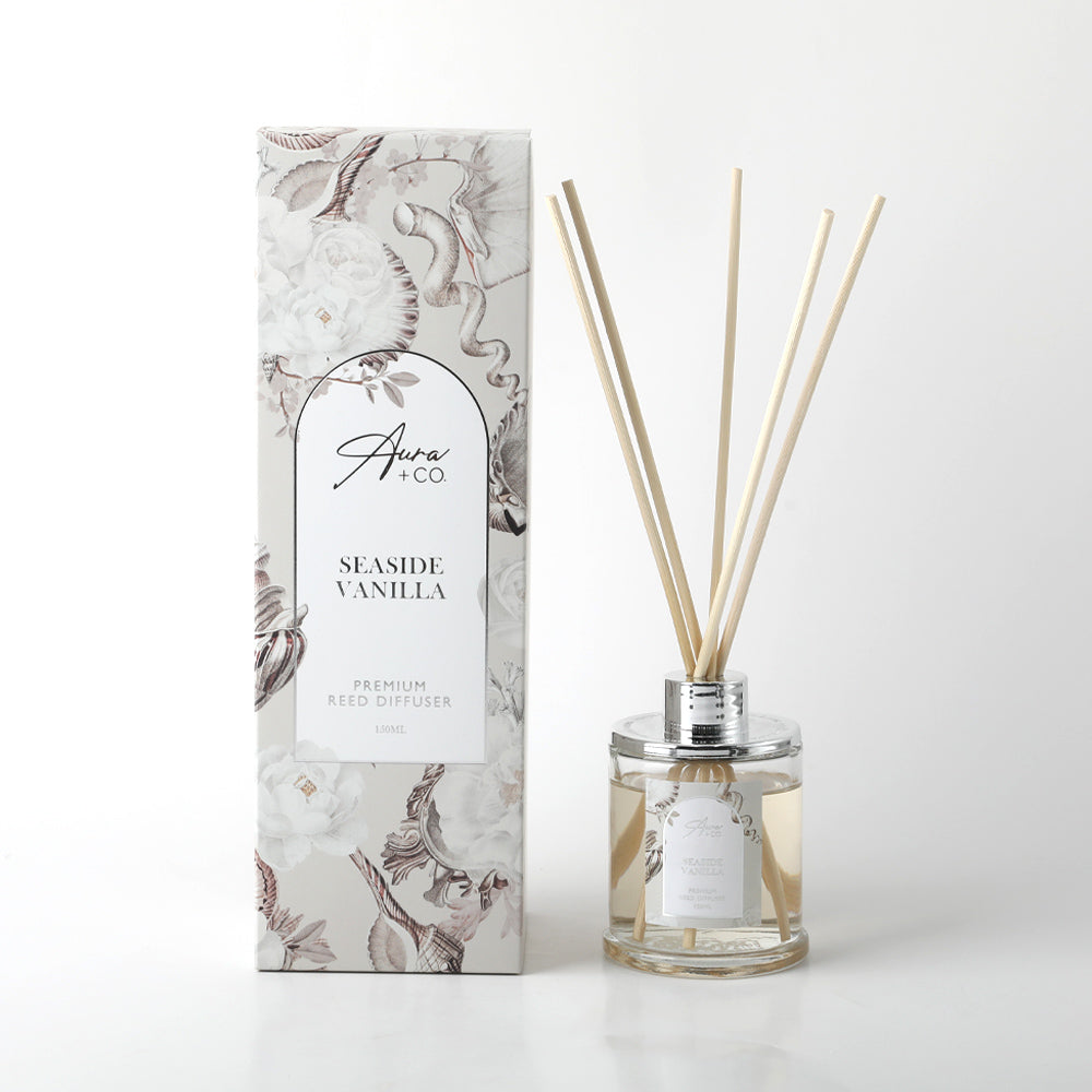 Clear glass bottle with silver collar; Light beige liquid inside the bottle; Thin natural reed sticks included; Decorative box with floral and seashell pattern in neutral tones;