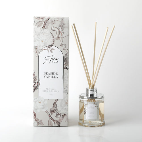 Clear glass bottle with silver collar; Light beige liquid inside the bottle; Thin natural reed sticks included; Decorative box with floral and seashell pattern in neutral tones;