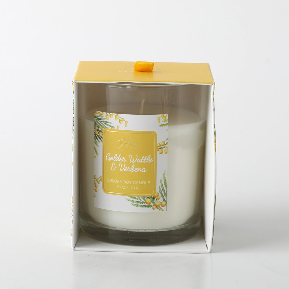 white candle in clear glass holder; yellow and white floral label with golden wattle illustration; packaged in white folded box with yellow top; yellow ribbon pull tab on top of box;