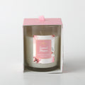 white candle in clear glass container; pink floral label with gumnut blossom illustration; pink cardboard box with front window; pink fabric ribbon pull tab on top;