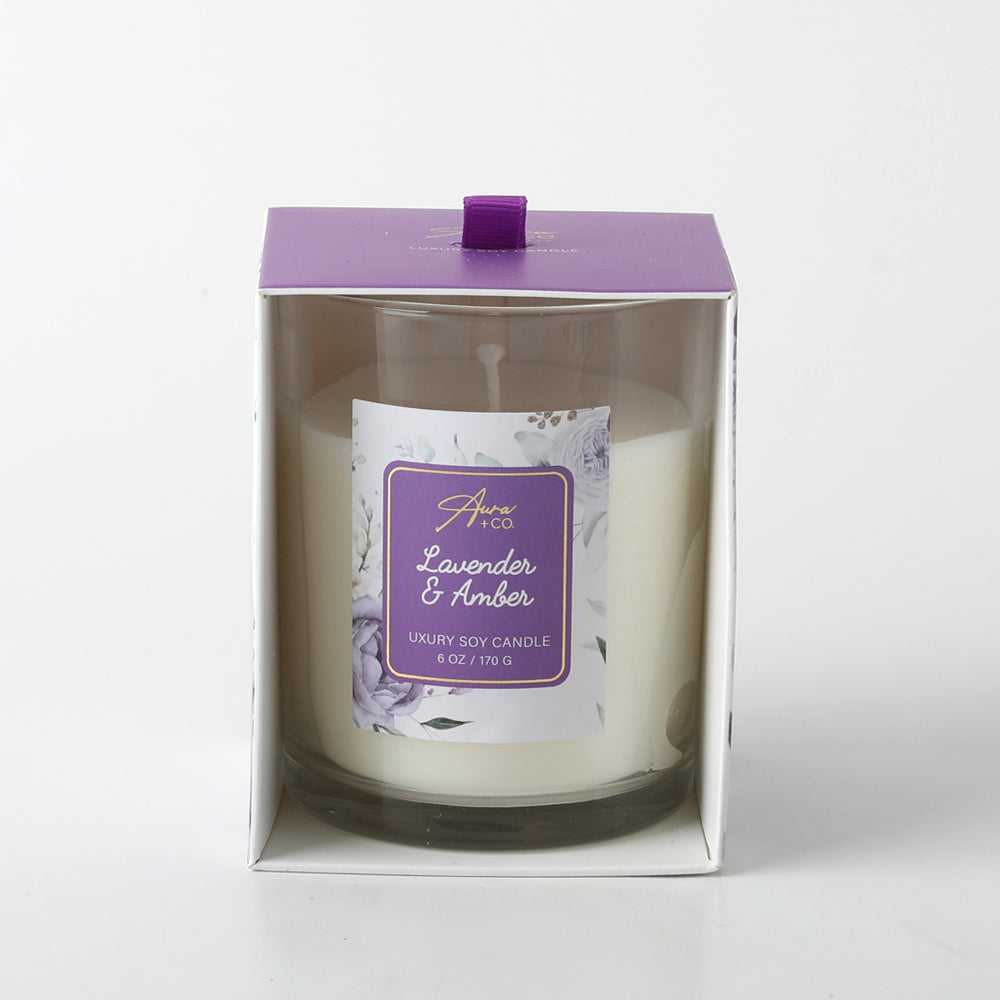 white candle in clear glass jar; purple label with floral design; purple box with pull tab; wax appears smooth and creamy;