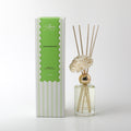 200ml clear glass bottle with pale yellow liquid; gold coloured collar around bottle neck; five natural wood reeds inserted in bottle; white foam flower attached at bottle neck; box packaging with green and white vertical stripes;
