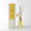 clear glass bottle with gold-coloured neck; yellow liquid inside; six natural reeds inserted; white foam flower decoration; packaging box with yellow and white stripes;