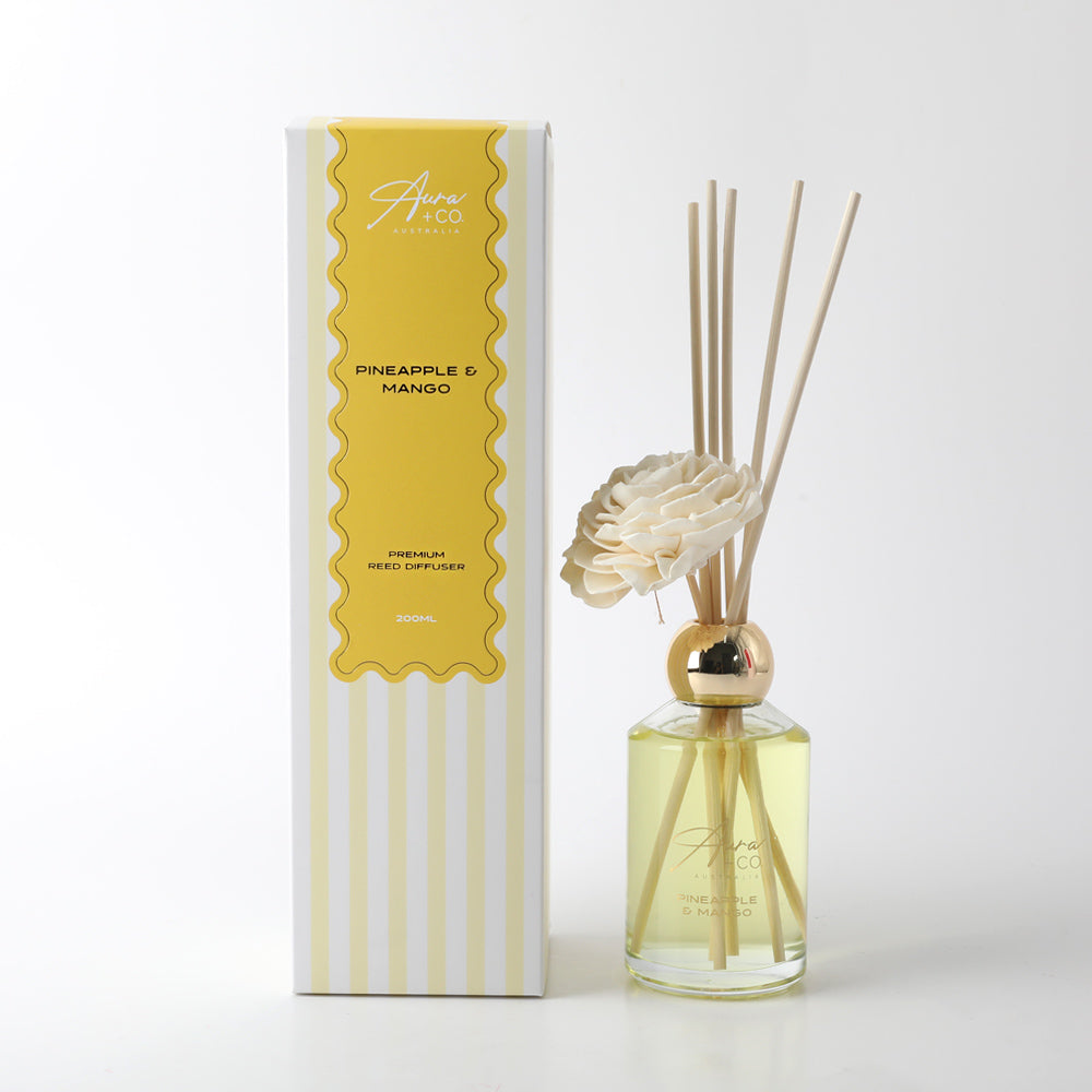 clear glass bottle with gold-coloured neck; yellow liquid inside; six natural reeds inserted; white foam flower decoration; packaging box with yellow and white stripes;