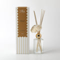 Clear glass bottle with gold collar; Decorative cream-coloured foam flower; Several light wooden reed sticks; Packaging box with beige and white stripes; Label with vanilla & caramel text;