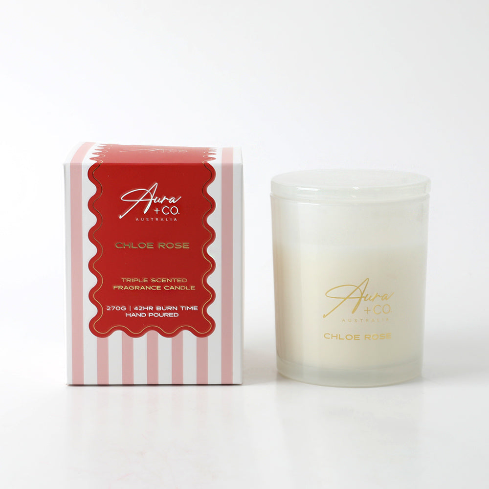 Frosted glass container with gold logo; White candle wax inside; Clear glass lid; Box with pink and white stripes and red label;