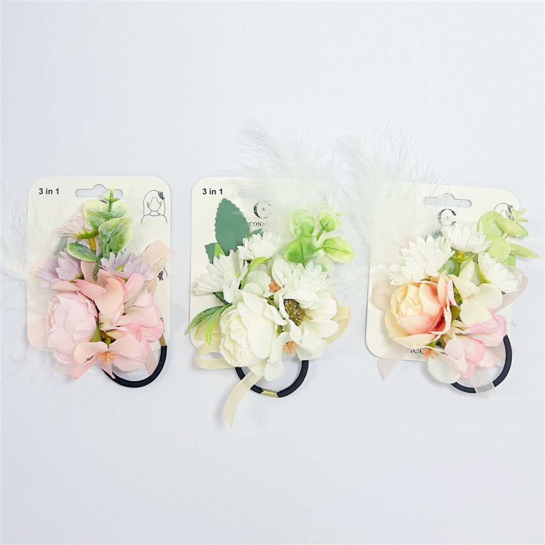 Artificial flower clusters in pastel pink and white; Mixed green leaves and foliage details; White feather accents attached to each piece; Mounted on backing cards labelled “3 in 1”; Black elastic loop at the base of each accessory;