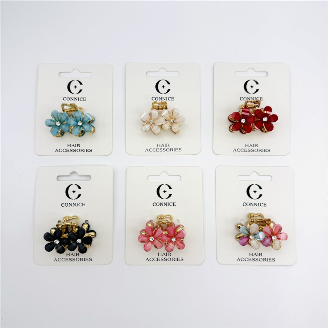Small flower-shaped hair claw clip; Gold-tone alloy claw base; Petal-style flowers with central rhinestone detail; Mounted on branded backing card labelled "Connice" and "Hair Accessories"; Shown in several assorted colours including blue, cream, red, black, pink and multicolour;