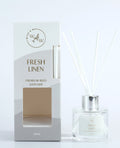 Clear round glass bottle; Silver-coloured cap; White reed sticks; Light grey and white packaging with cut-out window; Label and box text show 'Fresh Linen' scent;