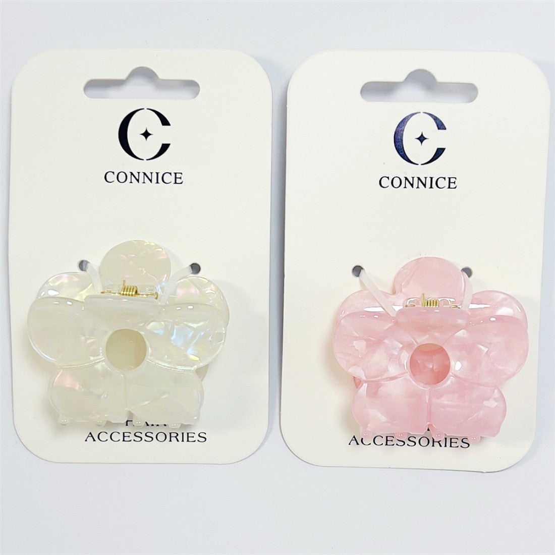 Flower-shaped claw clip design; One clip in pearlescent white, one in light pink; Glossy acrylic finish with marbled effect; Gold-tone metal spring mechanism; Mounted on white CONNICE branded backing cards;