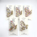 Gold-tone butterfly-shaped claw clip; Decorated with small flower beads and rhinestones; Iridescent and pastel pink accents; Mounted on white branded backing card; Approximate length around 7.5cm;