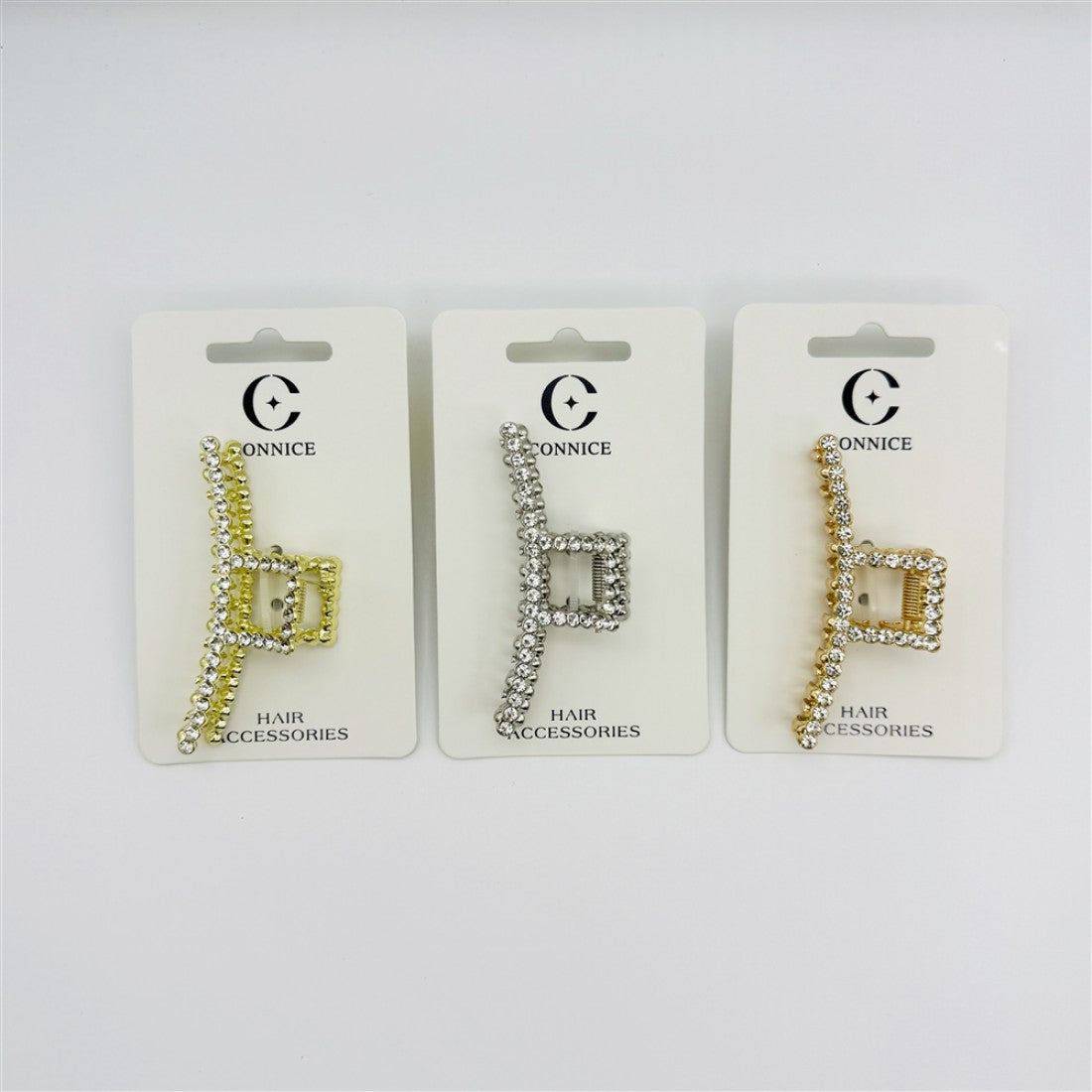 Rectangular claw clip with open geometric shape; Covered in clear rhinestones along the frame; Metallic alloy finish in light and gold tones shown; Packaged on white backing card labelled hair accessories;