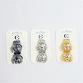 Two small claw clips mounted on white branded backing card; Clips shown in three metallic colours: black, silver and gold; Rounded claw shape with interlocking teeth; Glossy metal-look finish on each clip;