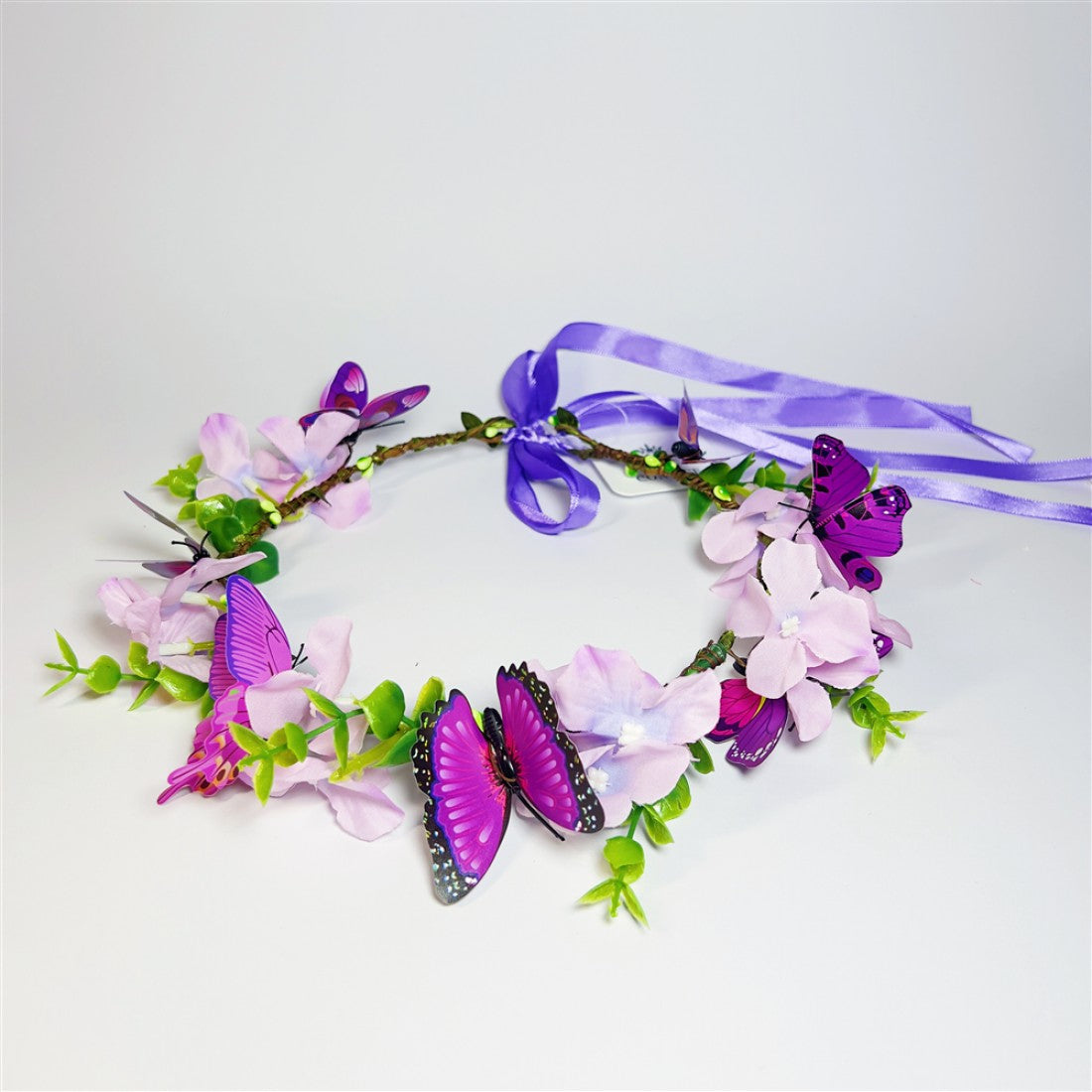 Purple satin ribbon tie at the back; Pink and purple artificial flowers around the ring; Green leaf sprigs along the wreath; Purple butterfly decorations attached to the flowers;