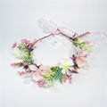 Wreath style floral crown with circular shape; Mixed pastel flowers in pink, cream and yellow tones; Green foliage and small berry-like accents; Pink sheer ribbon tie at the back; Attached branded swing tag on the wreath;