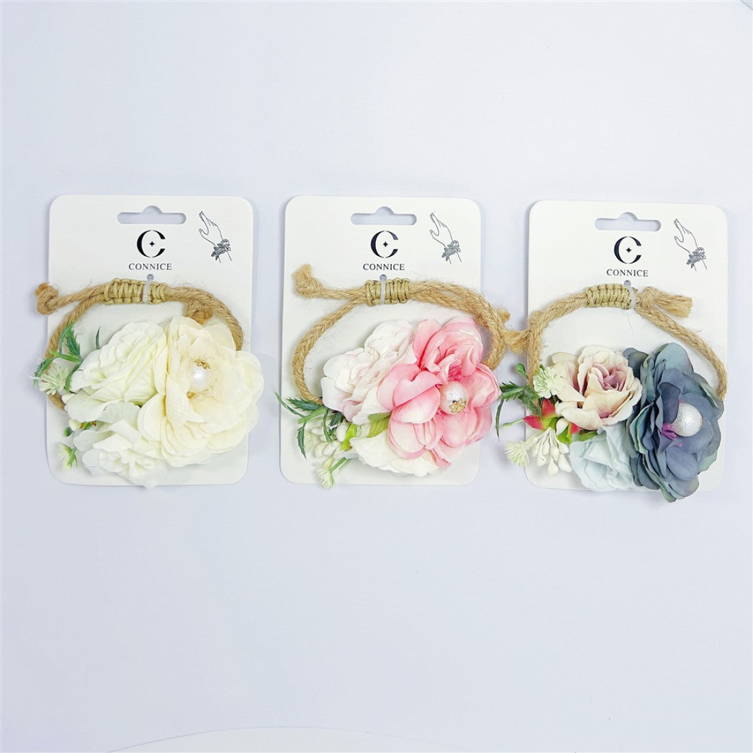 Artificial flower wrist corsage on branded backing card; Assorted soft colours including cream, pink and grey tones; Rustic twine loop and wrap used as wrist band; Includes faux greenery and small filler flowers;