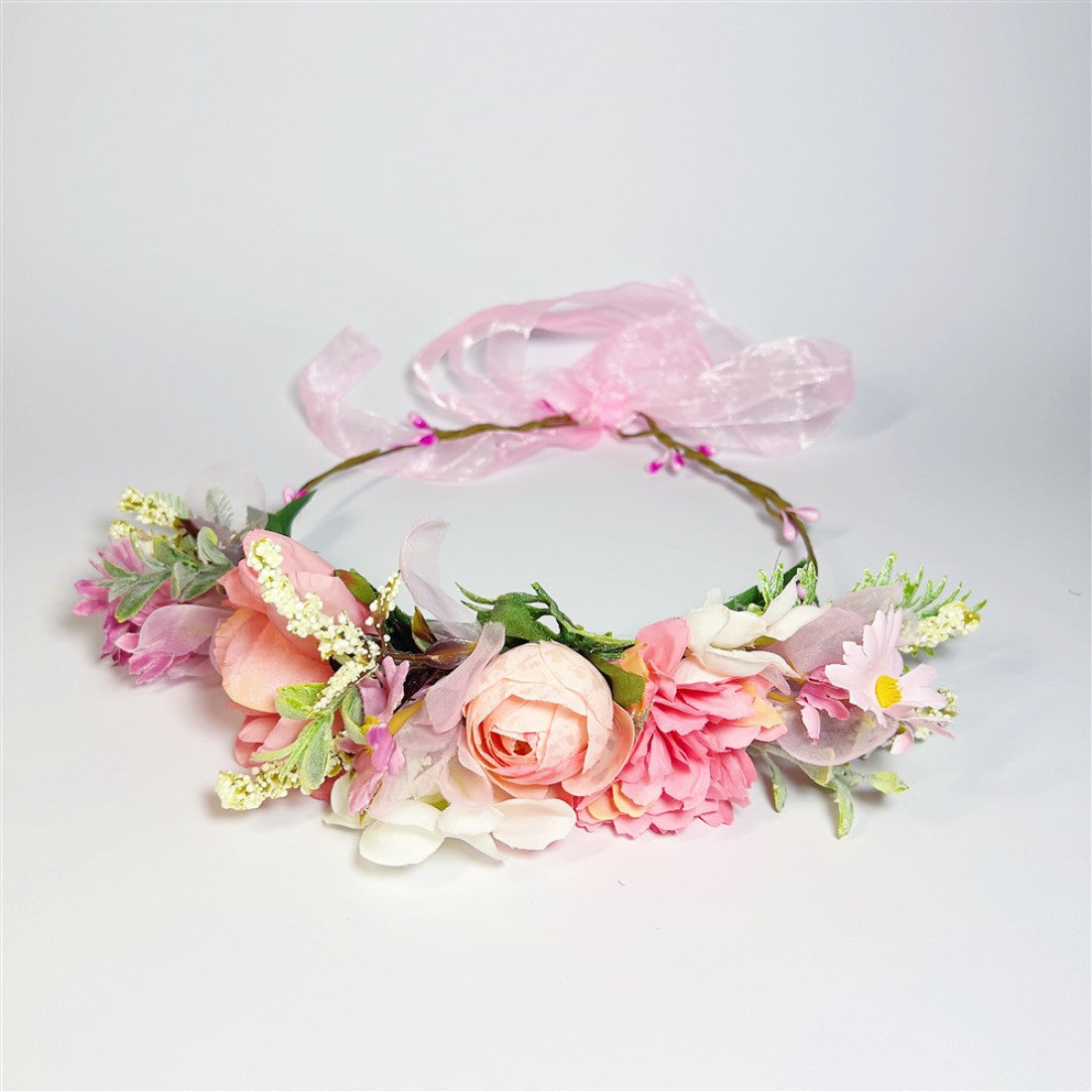 Circular flower crown design; Pink, white and peach artificial flowers; Green foliage accents; Sheer pink ribbon tie at the back;