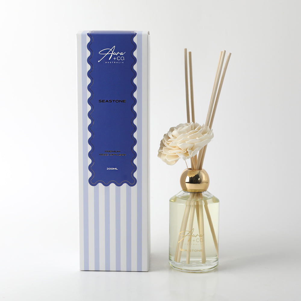 Clear glass bottle with gold collar; Cream foam flower decoration; Light yellow diffuser liquid; Striped blue and white packaging box; Reed diffuser sticks included;
