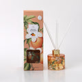 Clear round glass bottle with orange and white floral print; Orange-coloured liquid inside diffuser; Gold-coloured ring around bottle neck; Packaged in a peach box with orange and white flower illustrations;