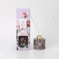 100ml clear round glass diffuser bottle with floral print; gold-coloured neck collar; five white diffuser reeds; packaging box with purple background and rose illustrations;