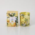 yellow glass holder with lemon and green leaf designs; matching boxed packaging with lemon and floral print; white candle wax inside glass holder;