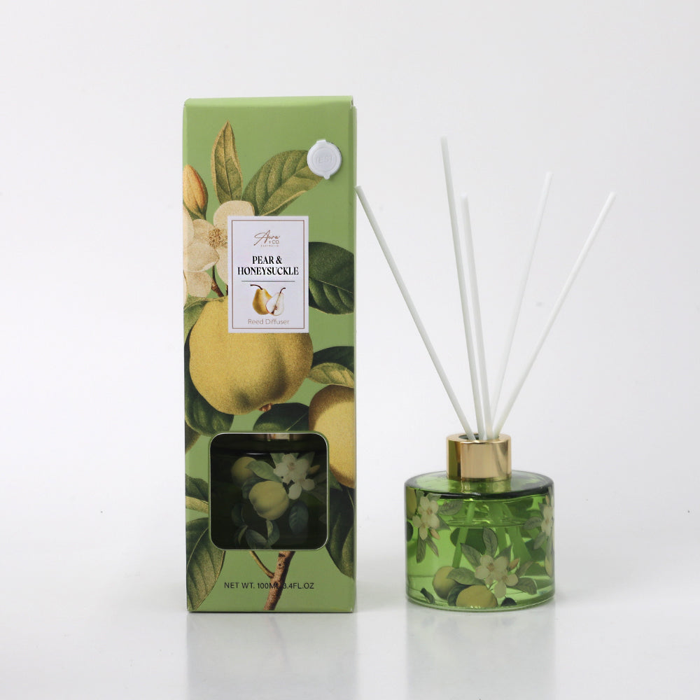 green glass bottle with botanical pear and flower print; gold coloured collar on diffuser bottle; white reed sticks inserted in the diffuser; outer box with matching botanical pear and flower design; green and gold colour scheme on packaging;