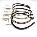 Slim plastic headbands with braided faux leather outer; Mix of colours including pink, cream, beige, tan and black; Inner side has small teeth for grip; Ends wrapped with black fabric for comfort; Each headband displayed on white branded hang card;