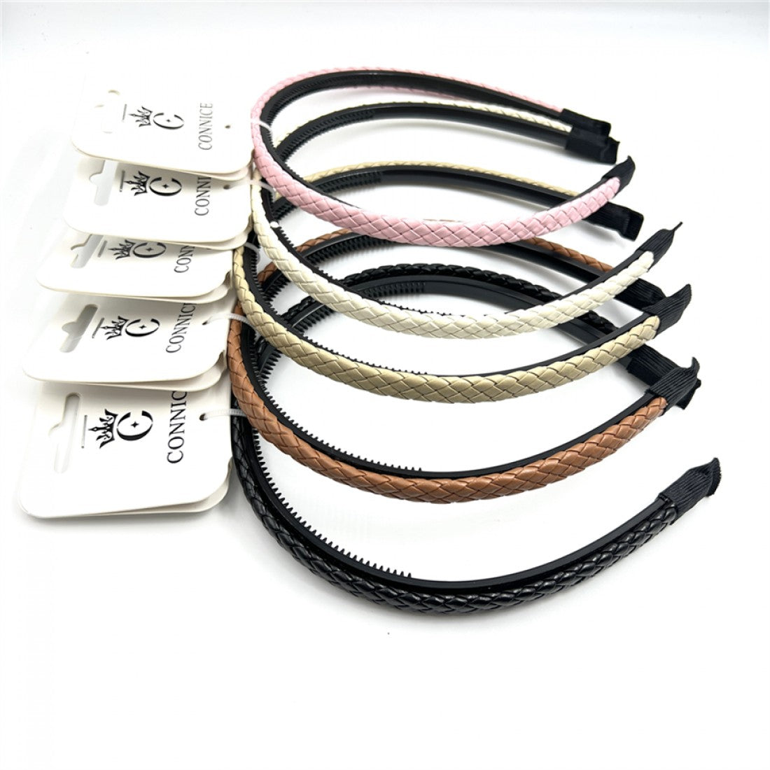 Slim plastic headbands with braided faux leather outer; Mix of colours including pink, cream, beige, tan and black; Inner side has small teeth for grip; Ends wrapped with black fabric for comfort; Each headband displayed on white branded hang card;