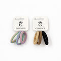 Braided elastic hair ties in looped bands; One set in pastel rainbow tones with purple and green; One set in beige, tan and black colours; Mounted on white CONNICE branded cards;