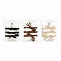Braided hair ties shown in black, brown and beige tones; Gold-coloured metal tips at the ends of each tie; Each colour set displayed on white branded backing cards; Looped and knotted designs visible on the ties;