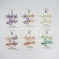 Shimmery translucent butterfly-shaped clips; Pastel gradient colours including purple, pink, yellow and green tones; Clips presented on white backing cards labelled "Hair Accessories"; Each card shows a set of three butterfly hair clips;