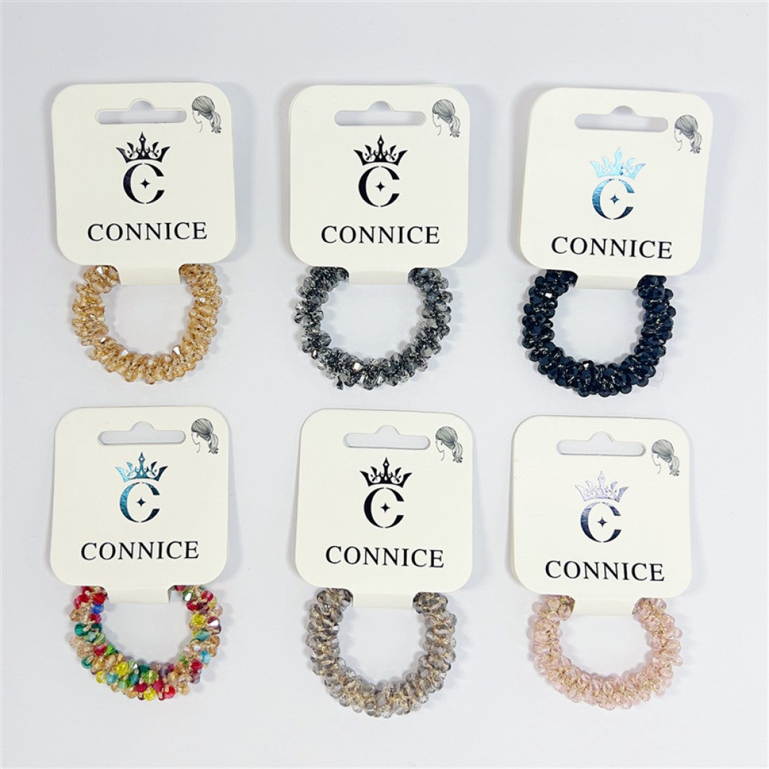 Coiled spiral hair tie design; Clear and coloured faceted beads creating a crystal look; Multiple colour options shown including gold, dark blue, multicolour and neutrals; Each hair tie displayed on white CONNICE branded card backing;