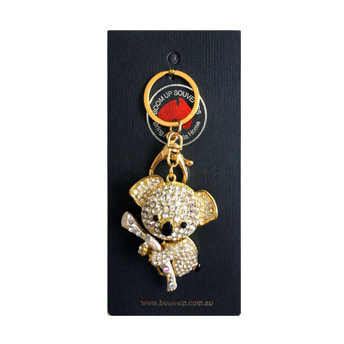 gold-tone koala shape keyring; covered in clear diamond-like stones; koala holding a branch; attached to gold split ring and clip; packaged on black branded card;