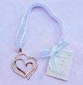 gold-coloured double heart shape; rhinestone embellishments on one heart; white hanging ribbon; attached gift tag with 'Best Wishes'; matte lavender background;