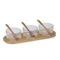 three transparent ribbed glass bowls; each bowl has a small wooden spoon; all items rest on a long wooden tray; natural wood colour and texture; compact rectangular tray shape;
