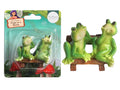 Two green frogs sitting on a brown bench; Bench has a wood-like texture; Figurines are made of resin or plastic; Packaging includes a cardboard backing with fairy garden theme;