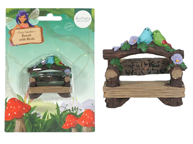 Small bench with wood texture; Two colourful birds (blue and green) on top; Floral decorations in purple and green; Sign with text 'Fairies Welcome';