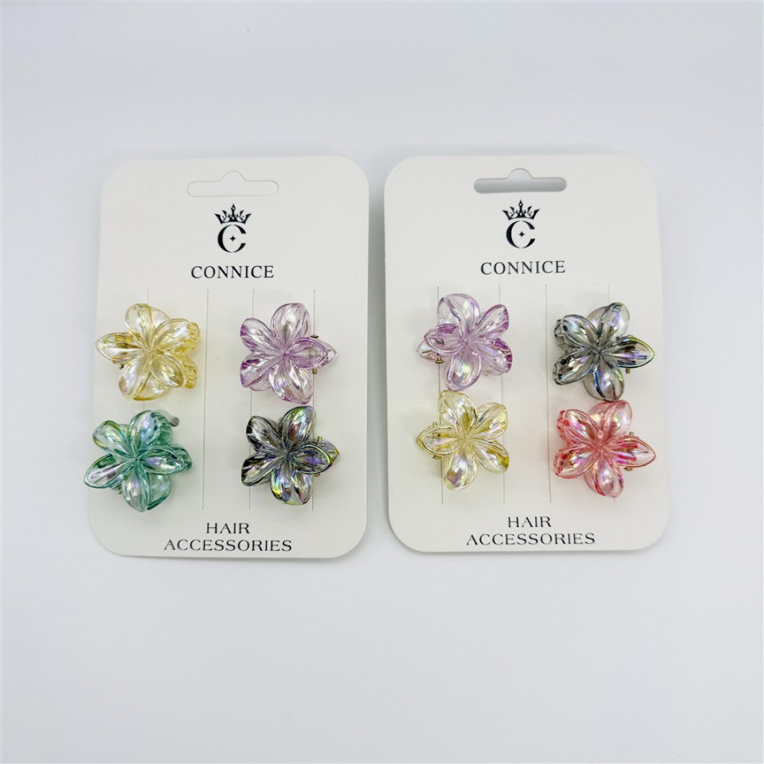 Set of four small flower-shaped claw clips; Iridescent, gradient plastic in assorted pastel tones; Mounted on white branded backing card; Frangipani-style five-petal design;