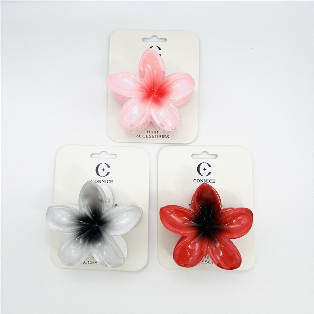 Frangipani-shaped five-petal flower design; Glossy plastic material; Seen in pink, red and white with darker centres; Mounted on branded backing card labelled as hair accessories;