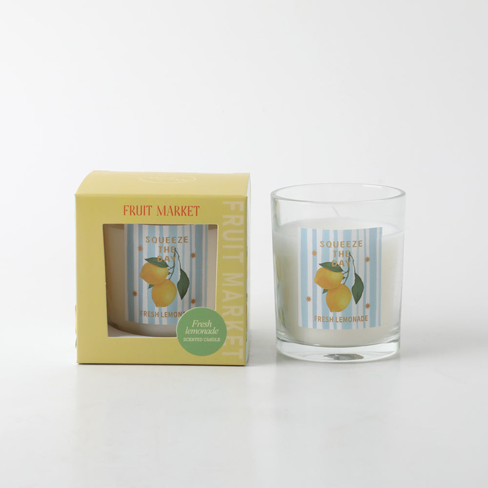 Yellow packaging box with window showing candle; Clear glass container with candle inside; Label on candle with lemons and blue stripes; Green sticker on box indicating 'Fresh lemonade' scent;