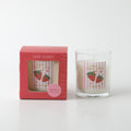 clear glass jar; white candle wax; pink and white striped label with strawberries; red packaging box; gold text on label;