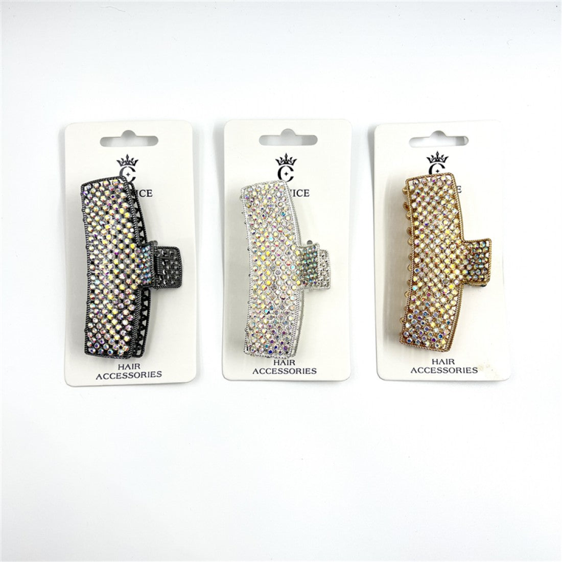 Rectangular claw clip shape; Covered in small rhinestones; Shown in metallic tones including black, silver and gold; Packaged on white backing card labelled "Hair Accessories";