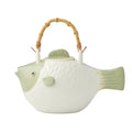 Fish-shaped ceramic teapot; Bamboo-style curved handle; White body with sage green accents on fins and face; Textured fish scale details on body; Lid with a small fin-shaped handle;