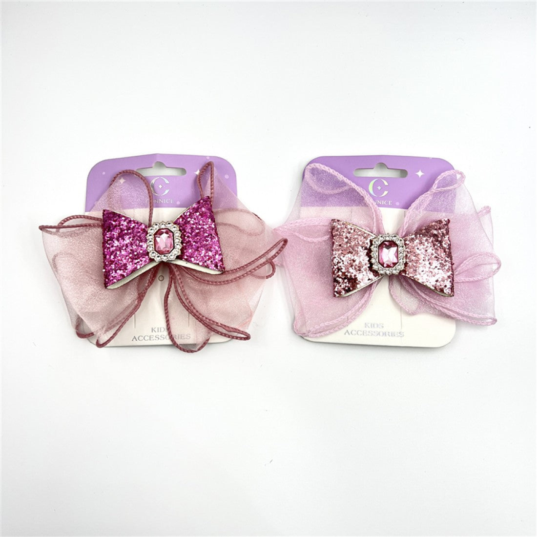 Glitter-covered central bow in pink tones; Clear gem embellishment set in a small frame; Large layered sheer ribbon bow backing; Packaged on purple and white backing card labelled kids accessories;