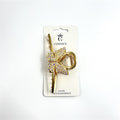 Gold-tone metal hair claw clip; Butterfly shape detail at centre; Butterfly covered in small iridescent crystals; Mounted on branded Connice hair accessories card; Long crossed bar design with teeth for gripping hair;